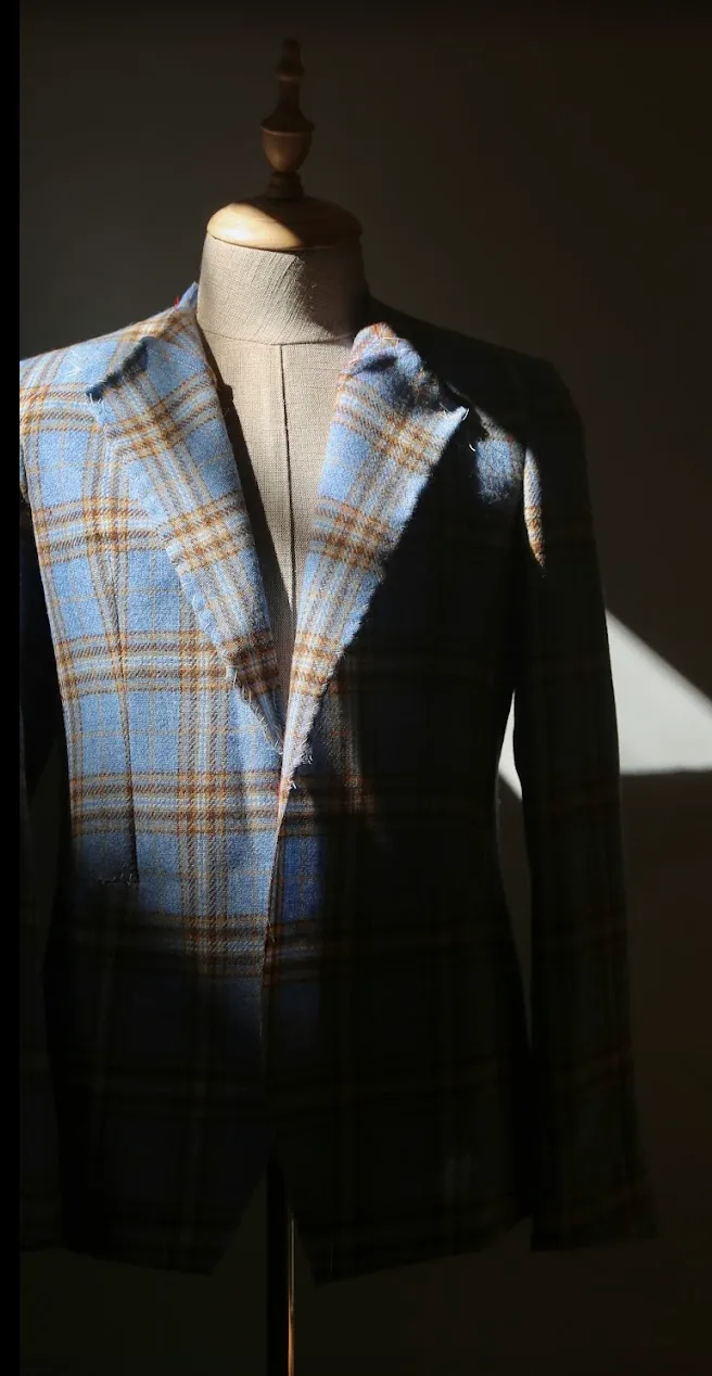 Blazer de cuadros en azul y tostado sobre maniquí de sastre, con las solapas sin rematar