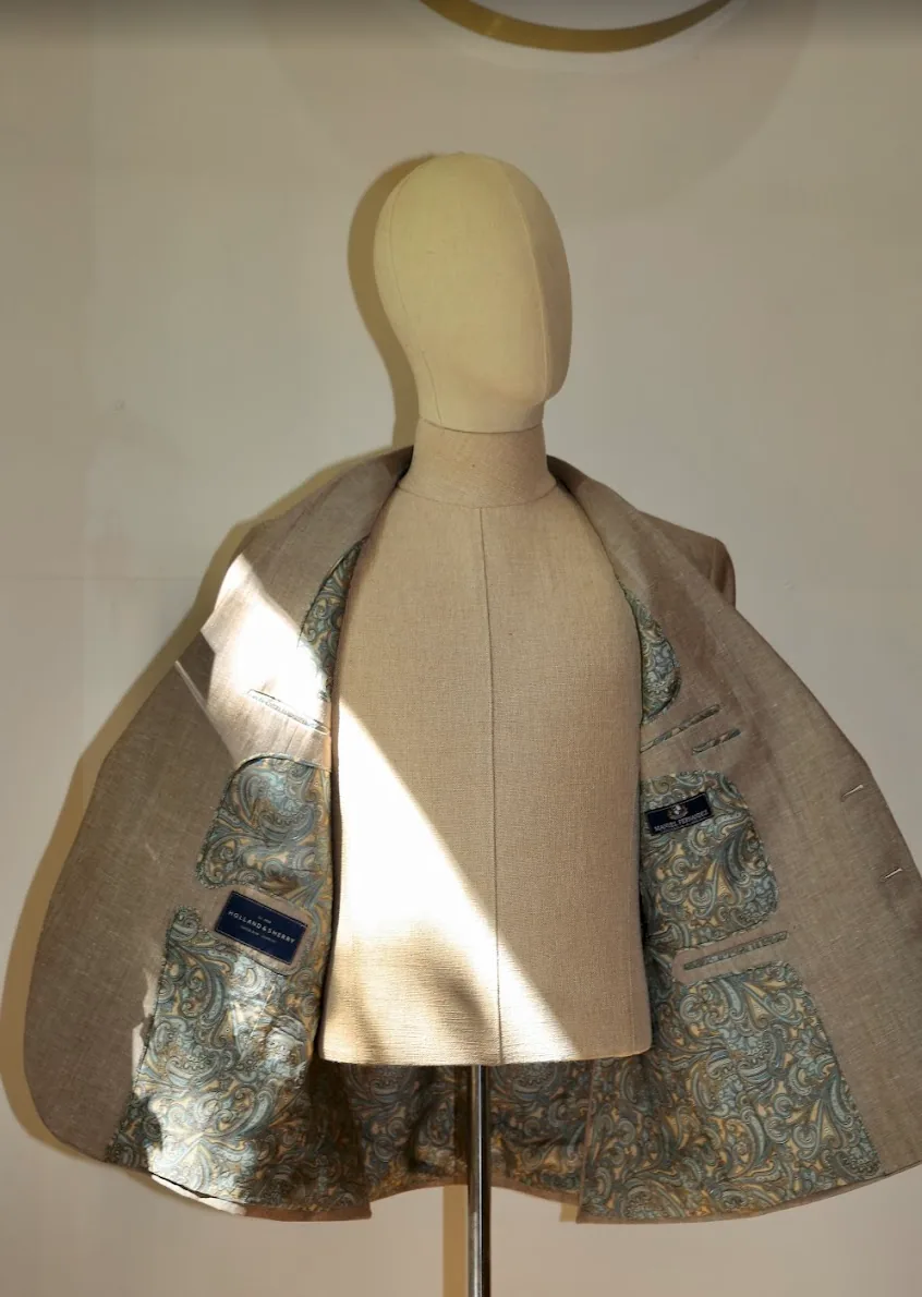 Chaqueta de lino beige abierta sobre maniquí, con el forro de paisley verde y dorado a la vista