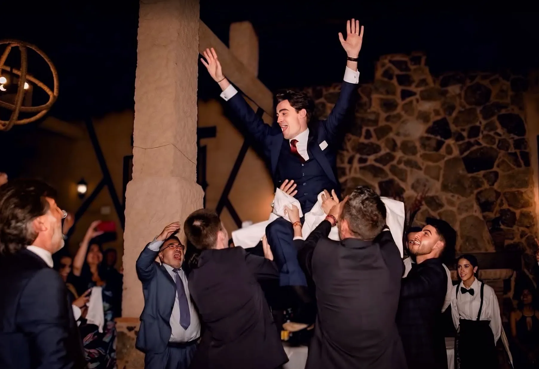 Novio con traje azul marino de tres piezas, en volandas durante la celebración de su boda